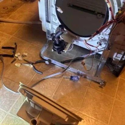 Washing machine taken apart on the floor with the drum, wiring and pump exposed